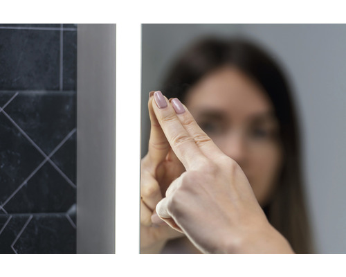 Frau berührt einen beleuchteten Badezimmerspiegel