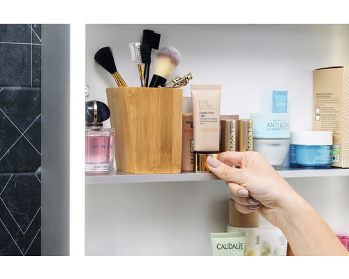 Badezimmerszene mit Kosmetikprodukten, Make-up-Pinsel und einem Holzbehälter in einem Spiegelschrank.