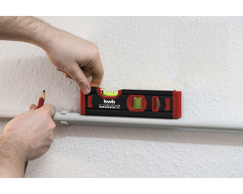 Eine Wasserwaage wird mit einem Bleistift auf einer Oberfläche ausgerichtet.