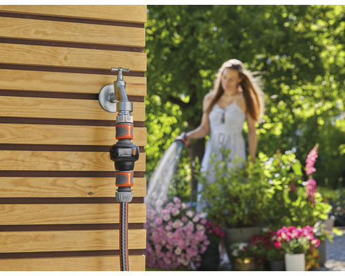 Compteur d''eau d''arrosage sur robinet avec une femme en arrière-plan arrosant le jardin