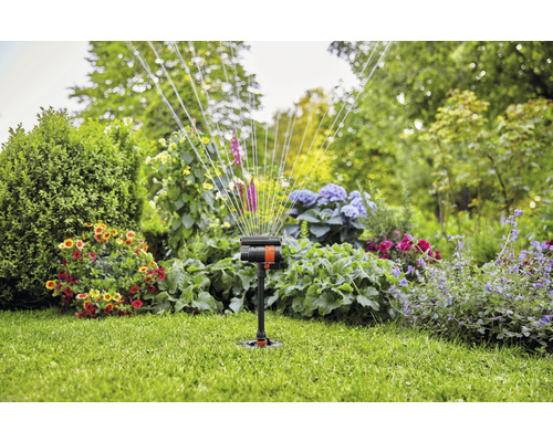 Arroseur de jardin en marche sur une pelouse avec des parterres de fleurs en arrière-plan.