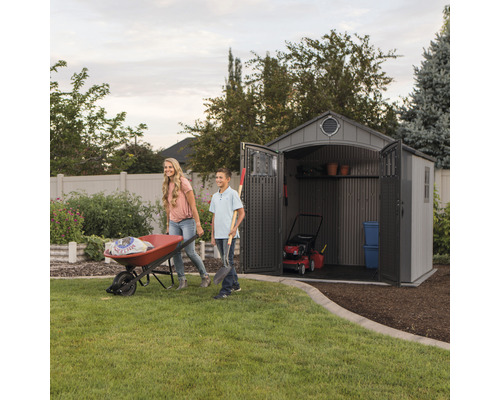 Scène de jardin avec une remise de jardin, une brouette et deux personnes faisant du jardinage