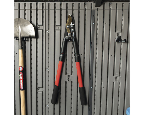 Des outils de jardin tels qu''une bêche et un taille-haie sont accrochés à un mur gris