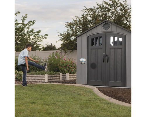 Scène avec un garçon frappant un ballon contre une remise de jardin grise dans le jardin
