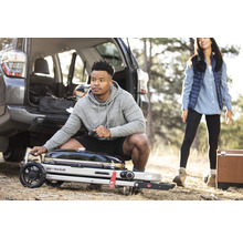 Szene mit einem tragbaren Weber Traveler Grill, einem Mann und einer Frau im Freien neben einem Auto.