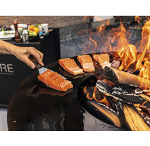Préparation de saumon sur une plaque de cuisson au feu de bois.