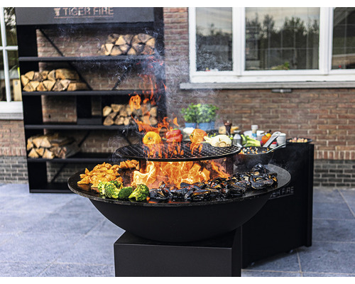 Tiger Fire Grill mit Holzregal und zubereiteten Speisen im Aussenbereich.
