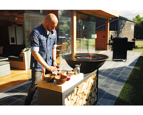 Un homme prépare de la viande sur un anneau de feu pour barbecue Tiger Grill dans le jardin.