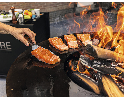 Préparation de saumon sur une plaque de cuisson avec un feu de bois.
