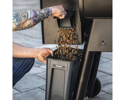 Eine Person füllt Holzpellets in einen Pelletbehälter an einem Grill