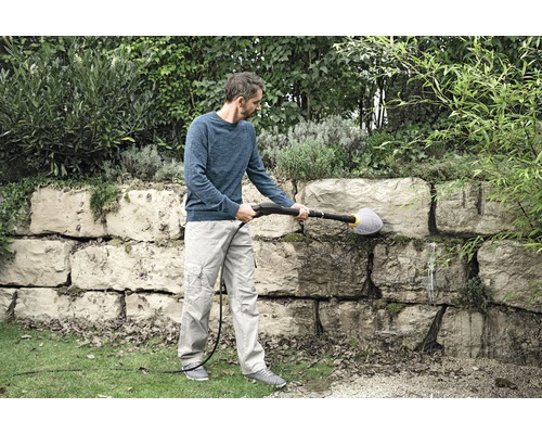 Un homme nettoie un mur de pierre avec une brosse et un nettoyeur haute pression.