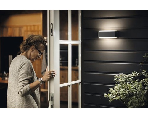 Frau öffnet Haustür mit Aussenwandleuchte