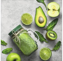 Grüner Smoothie in einem Glas mit Deckel, umgeben von Limetten, Avocado, Apfel, Kiwi und Spinat.