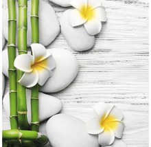 Dekorative Anordnung mit Bambusstäben, weissen Steinen und Frangipani Blüten auf einem Holztisch.