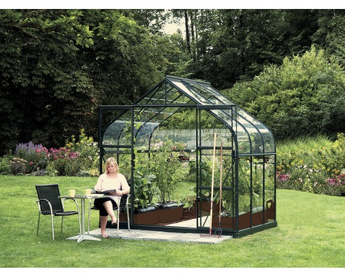 Gewächshaus Vitavia Diana 5000 Einscheibensicherheitsglas 3 mm 264x195 cm grün Frau liest vor einem Gewächshaus mit Pflanzen auf einer Wiese