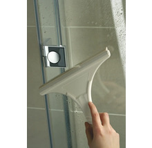 Une main essuie une paroi de douche avec une raclette de douche