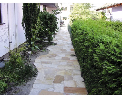 Gartenweg aus Natursteinplatten zwischen Haus und Hecke