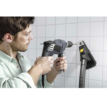 Un homme perce un trou dans un mur carrelé avec une perceuse à côté d''un aspirateur