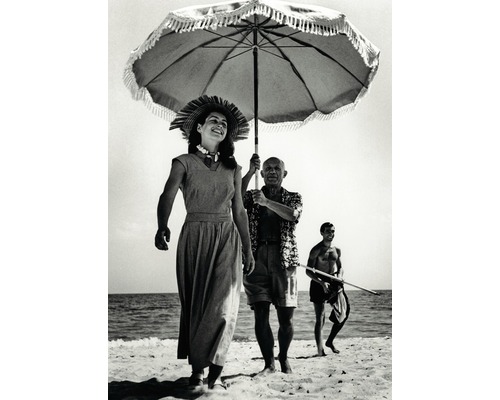 Photo en noir et blanc d''une femme marchant sur la plage avec un homme tenant un parasol et un homme tenant une lance