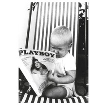 Ein Kind sitzt auf einem gestreiften Stuhl und liest ein Playboy-Magazin.