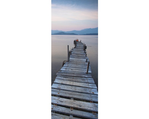 Ein langer, alter Holzsteg führt in ein Gewässer mit Bergen im Hintergrund.