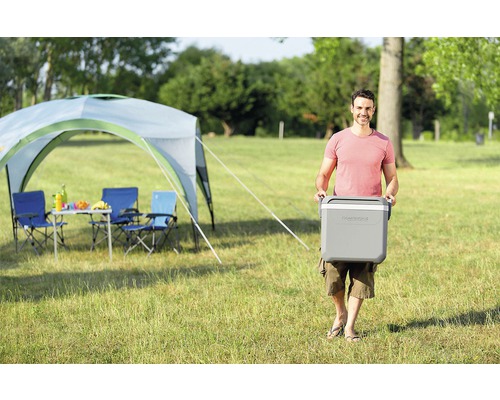 Mann trägt Kühlbox beim Camping mit Zelt und Campingmöbeln
