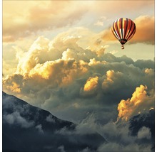 Heissluftballon über bewaldeten Bergen unter einem bewölkten Himmel