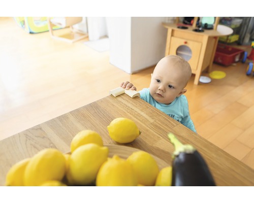 Kleinkind steht an einem Tisch mit Eckenschutz, Zitronen und einer Aubergine