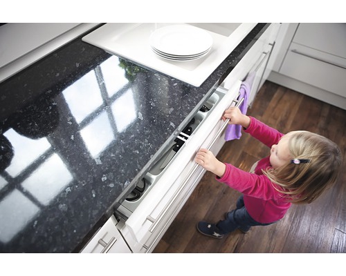 Ein kleines Kind öffnet eine Küchenschublade mit einem Messerblock.