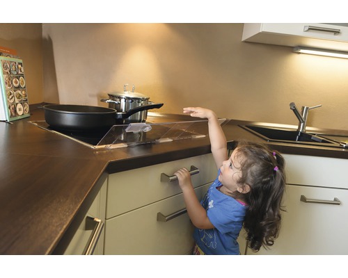 Un enfant atteint une cuisinière avec une protection de plaque de cuisson dans la cuisine