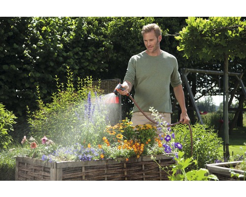 Mann bewässert Blumen in einem Hochbeet mit einem Gartenschlauch
