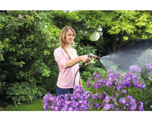 Frau bewässert Blumen mit einem Gartenschlauch im Garten.