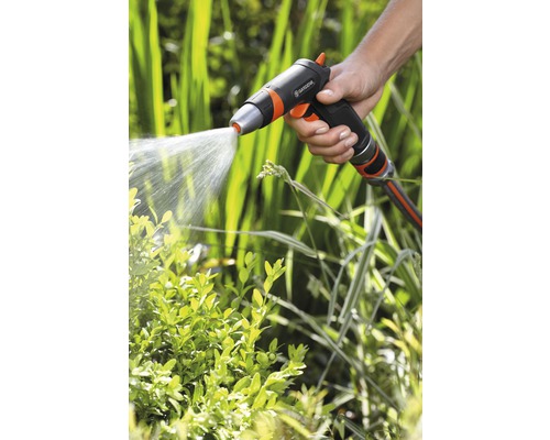 Une main tient un pulvérisateur de jardin qui arrose les plantes.