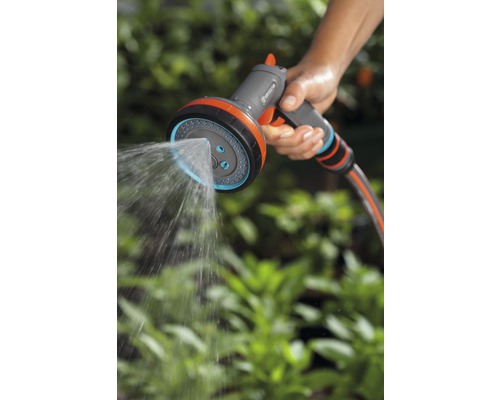 Une personne tient un pulvérisateur de jardin multifonction Gardena qui pulvérise de l''eau.