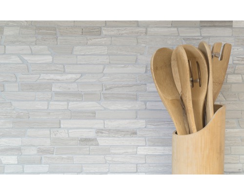 Ustensiles de cuisine en bois dans un support devant un mur en pierre