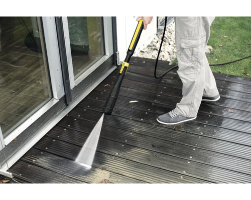 Person reinigt Holzterrasse mit Hochdruckreiniger.