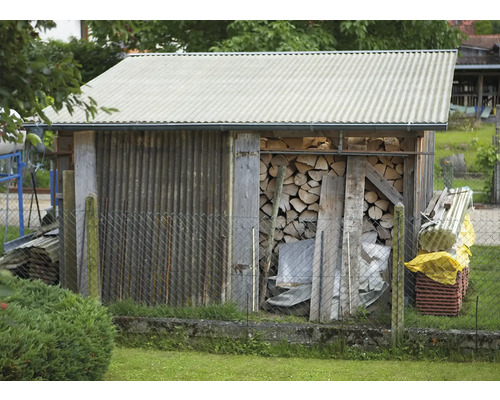 Abri à bois avec bois de chauffage et toit en tôle ondulée derrière une clôture en grillage
