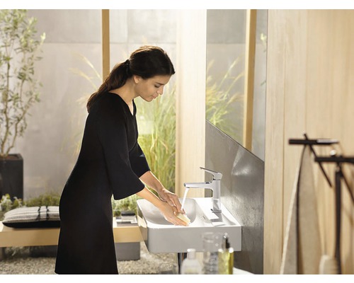 Une femme se lave les mains dans une salle de bains moderne avec une vasque à poser et un robinet.