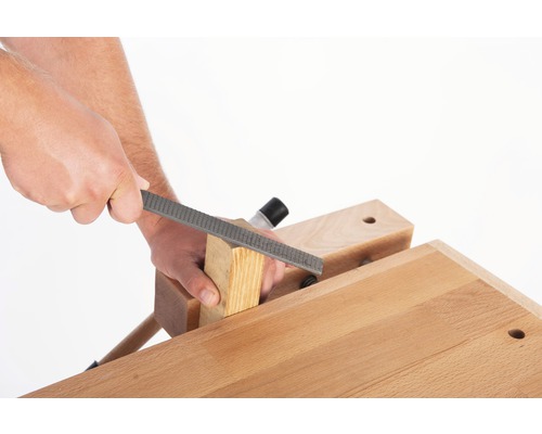 Artisan travaillant une pièce de bois avec une râpe à bois sur un établi