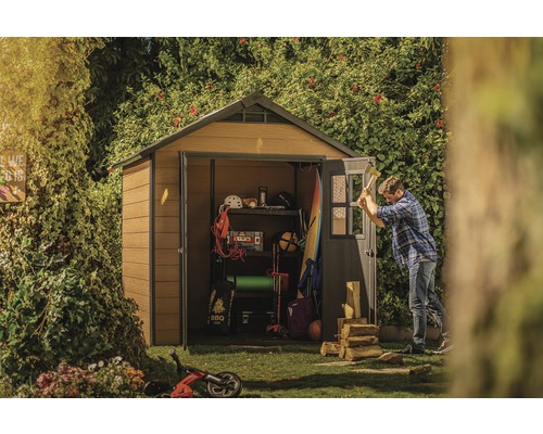 Gartenszene mit Gerätehaus, in dem Werkzeuge und Gartengeräte aufbewahrt werden, während ein Mann Holz hackt