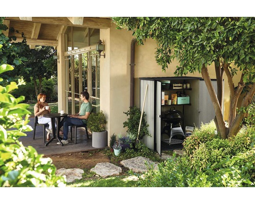 Scène de jardin avec une remise de jardin, des outils de jardinage et une femme assise et un homme assis