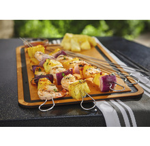 Brochettes grillées avec ananas, crevettes et oignon rouge sur une planche en bois.