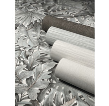 Trois rouleaux de papier peint sont posés sur un papier peint à motifs de plantes.