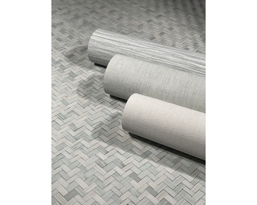 Trois rouleaux de papier peint avec différents motifs reposent sur un support tressé.