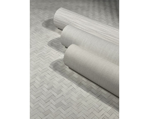 Drei Rollen textile Vliestapeten auf einem geflochtenen Untergrund.