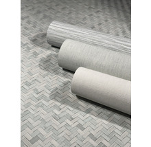 Drei Rollen Textiltapeten auf einem Boden mit Fischgrätmuster.