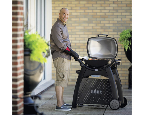 Un homme fait des grillades avec un barbecue électrique Weber en extérieur.