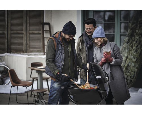 Eine Gruppe von Freunden grillt Gemüse im Wintergarten auf einem Kugelgrill.