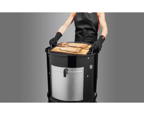 Frau mit Grillhandschuhen bereitet Fisch auf einem Holzkohlegrill zu