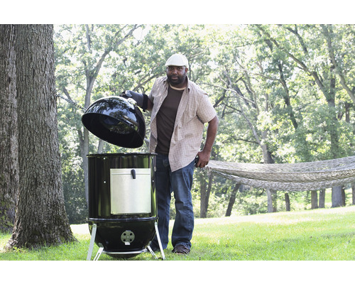 Mann öffnet einen runden Grill im Garten.